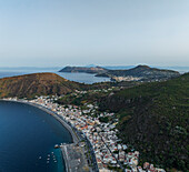 Luftaufnahme der kleinen Stadt Canneto entlang der Mittelmeerküste mit der Insel Vulcano im Hintergrund, Lipari, Äolische Inseln, Sizilien, Italien