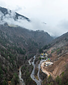 Luftaufnahme einer Hochgebirgsstraße, die sich durch ein nebliges Tal schlängelt, Karneid, Südtirol, Italien.
