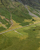 Luftaufnahme einer kurvenreichen Straße durch ein üppig grünes Tal, umgeben von majestätischen Bergen, Ballachulish, Vereinigtes Königreich