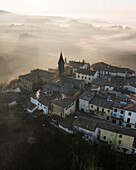 Aerial view of medieval village with historic architecture surrounded by fog and mist at sunrise, Piantravigne, Tuscany, Italy.