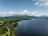 Aerial view of serene Loch Lomond surrounded by lush mountains and a tranquil sky, Trossachs National Park, Scotland.