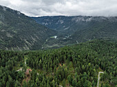 Luftaufnahme von üppig grünen Tälern und zerklüfteten Bergen unter bewölktem Himmel, Biberwier, Österreich.