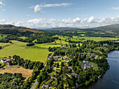 Aerial view of tranquil Loch Lomond surrounded by lush hills and picturesque village, Trossachs National Park, United Kingdom.