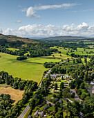 Aerial view of lush green fields and serene hills with trees and a winding road, Loch Lomond, Trossachs National Park, Scotland, United Kingdom.