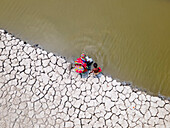 Aerial view of a coastal village facing drought with cracked earth and a community collecting water, Khulna, Bangladesh.