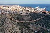 Aerial view of a fortress that has a wall connecting both sides of the valley, the Muralla de Jairán with the city in the background of Almeria, Andalucía, Spain.