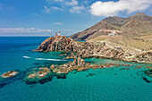 Aerial view of geological formation of volcanic rocks by the coast in the Cabo de Gata with a lighthouse and mountains in the background in Almería, Andalusia, Spain.