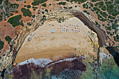 Aerial view of a beach area with umbrellas in a secluded cove only accessible by boat on the rocky coastline of Albufeira, Algarve, Portugal.