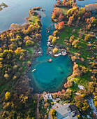 Aerial view of the serene Eye of Shegan karst spring surrounded by lush forest and vibrant autumn foliage, Bajze, Albania.