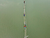 Aerial view of a serene coastal village with a traditional bridge and people fishing in a tranquil river, Khulna, Bangladesh.