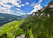 Luftaufnahme eines malerischen Bergtals mit üppigen grünen Feldern und einem beschaulichen Dorf, Heiligkreuz, Schweiz