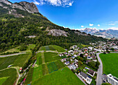 Luftaufnahme eines malerischen Dorfes, umgeben von üppigem Grün und Feldern mit Bergen im Hintergrund, Torkelfeld, Sargans, Schweiz