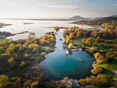 Aerial view of the serene Eye of Shegan karst spring surrounded by tranquil trees and picturesque mountains, Bajze, Albania.