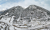 Aerial view of serene snowy mountains and a tranquil village surrounded by a rugged forest, Gurtnellen, Switzerland.