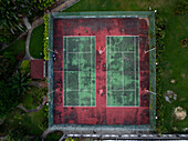 Luftaufnahme eines lebhaften Tennisplatzes mit Spielern in Aktion, umgeben von städtischer Architektur und üppiger Vegetation, Lagos, Nigeria.