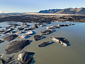 Aerial view of lake with icebergs covered with black volcanic ash in front of glacier tongue Skeidararjokull, Iceland.