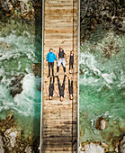 Aerial view of sporty family lying on wooden suspension bridge above a river.