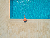 Luftaufnahme eines jungen Mädchens mit Sonnenhut, das am Swimmingpool sitzt, Sumartin, Insel Brac, Kroatien.