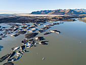 Aerial view of lake with icebergs covered with black volcanic ash in front of glacier tongue Skeidararjokull, Iceland.