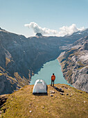 Aerial View of hiker with tent admiring view od Swiss Mountain Lake in Glarus, Switzerland.