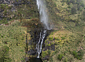 Aerial view of cascata do poco do bacalhau waterfall cascading down a lush green cliff surrounded by serene forest, Faja Grande, Portugal.