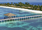 Aerial view of luxury resort on Ismehela Hera with turquoise waters and woman on jetty, Addu Atoll, Maldives.