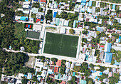Luftaufnahme einer üppig bewachsenen Insel mit Dächern und einem Fußballfeld, Thoddoo, Malediven.