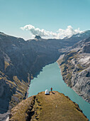 Aerial View of hiker with tent admiring view od Swiss Mountain Lake in Glarus, Switzerland.