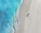 Luftaufnahme eines wunderschönen tropischen Strandes mit türkisfarbenem Wasser und einer Frau, die einen Schatten auf den Sand wirft, Vashafaru, Malediven