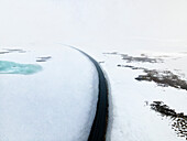 Luftaufnahme einer von Schnee und Eis umgebenen Winterstraße, Holmavik, Island.