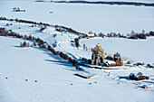 Aerial view of a picturesque snowy landscape with a traditional wooden church in a remote village, Karelia, Russia.