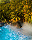 Aerial view of two girls on a paradise beach with white sand and palm trees in Mahe, Seychelles.