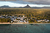 Aerial view of tranquil beach with boats, Rempart mountain, and hotels during golden hour, Flic en Flac, Mauritius.