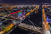 Aerial view of Samuel Beckett Bridge crossing the Liffey River at night with city skyline in background, Dublin, Ireland.
