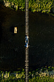 Aerial view of person lying down on rope bridge going over the river, Birstonas, Lithuania. Shot during sunset in Spring time.