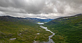 Luftaufnahme des Sees Vuolimus Gorsajavri und des sich windenden Flusses, umgeben von majestätischen Bergen und üppigen Tälern, Nationalpark Abisko, Schweden.