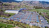 Aerial view of a scenic sports complex with parking lot and cars surrounded by mountains and greenery, Nelson, New Zealand.