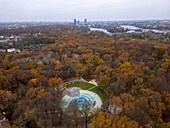 Aerial view of autumn colors in a tranquil park surrounded by trees and city skyline, Planterwald, Berlin, Germany.