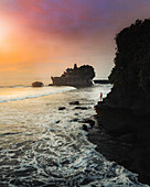 Aerial view of a person enjoying the view of Tanah Lot Temple at sunset in Bali, Indonesia.