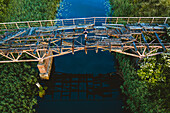 Aerial view of person lying down on old wooden collapsed bridge in Lithuanian countryside.