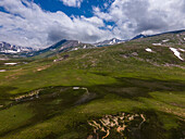 Aerial view of majestic snowy mountains and lush green grassland under cloudy skies, Sambaksar Pass, Gilgit Baltistan, Pakistan.