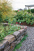 Strukturierter Garten mit Kiesweg, Natursteinmauer und Rosenbeeten