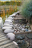 Barfussweg mit runden Steinen und Baumscheiben neben Teich