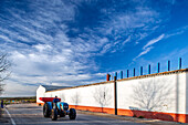 Carrión, Spain, Jan 21 2019, Blue tractor by long white red building, blue posts. Carrion, Seville, Andalusia, Spain.