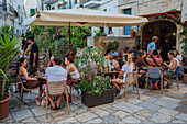 People enjoying lunch in a restaurant terrace surrounded by plants, Polignano a Mare, Italy