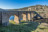Visitors admire the historic Roman bridge spanning the tranquil waters of Alcantara, showcasing stunning ancient architecture amid nature.