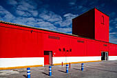 A modern, vibrant red building with white accents stands under a bright blue sky in Pilas, Seville, Andalusia, Spain.