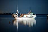 Stillness surrounds the fishing boat anchored in Punta del Moral, Ayamonte, as night envelops the tranquil waters of Andalusia.