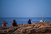 Menschen genießen die Aussicht auf den Sonnenuntergang am Pendma Chiatt (Pietra Piatta) mit einer Segelyacht im Hintergrund, Polignano a Mare, Apulien, Italien