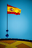 The vibrant flag of Spain waves proudly above the entrance gate at the April Fair in Seville, showcasing the festive atmosphere.